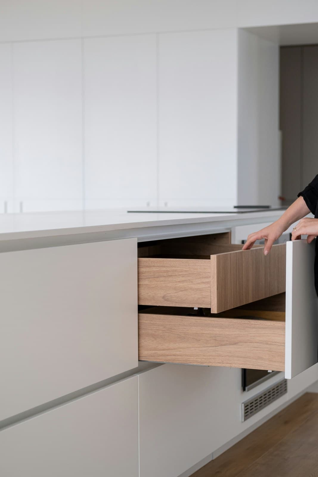 A hand opening a timber drawer in a white kitchen