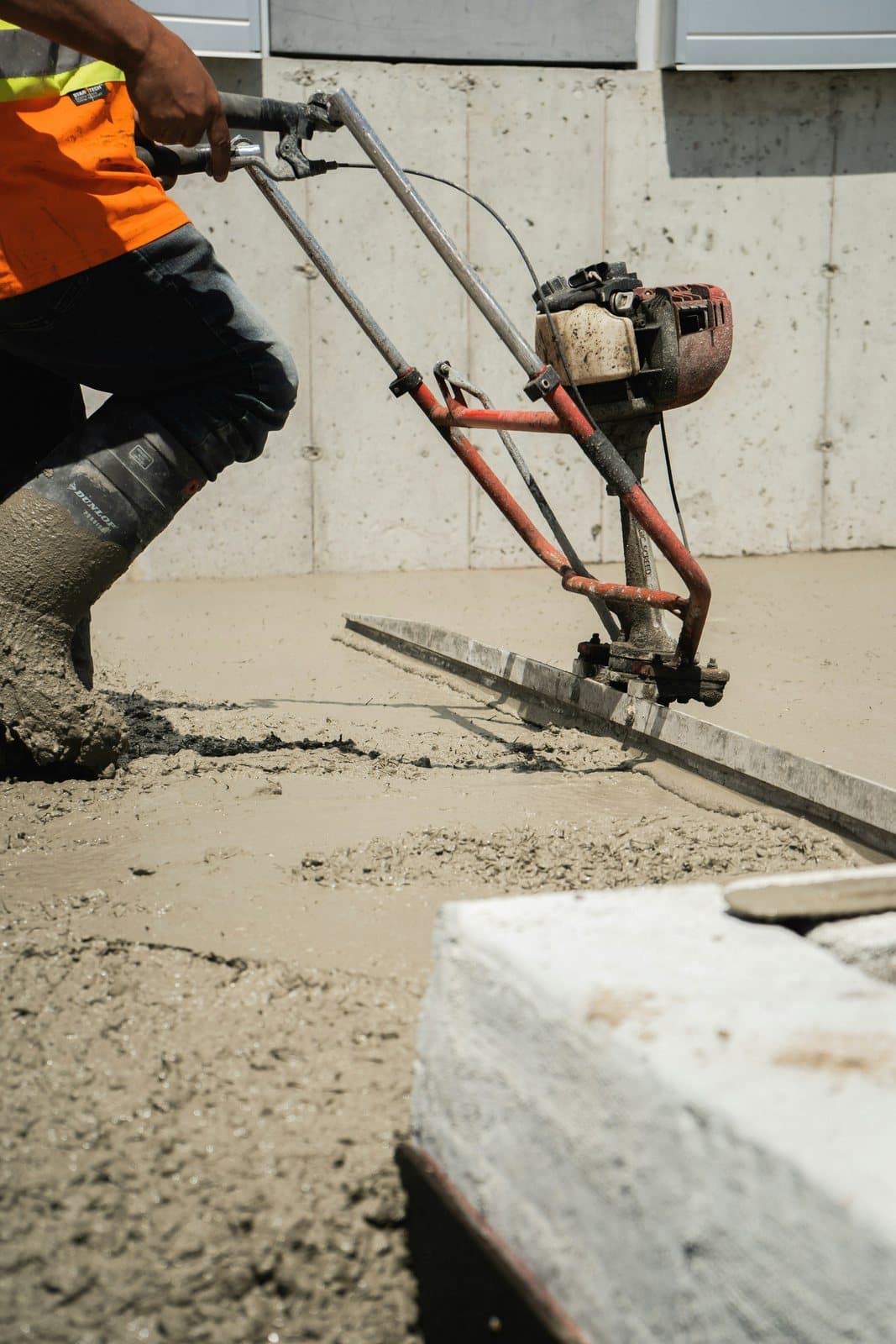 A power screed levelling a fresh concrete slab beside a concrete wall
