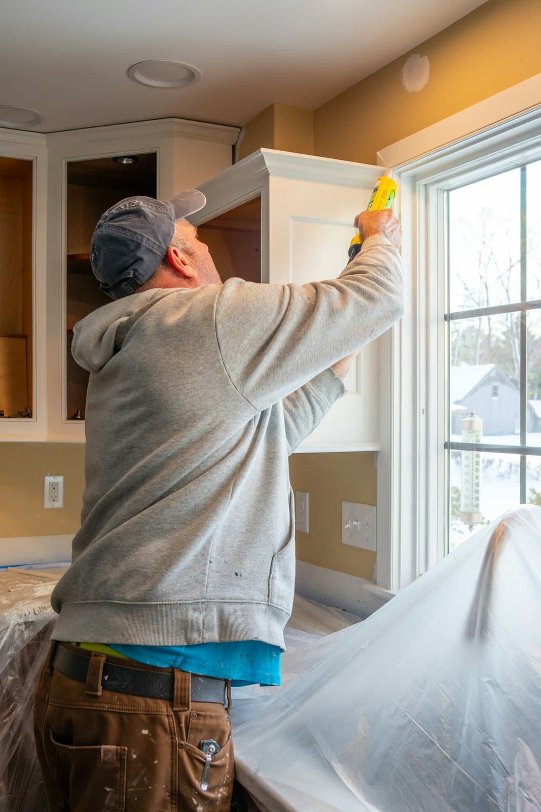 A painter on a step painting the trim above kitchen cupboards