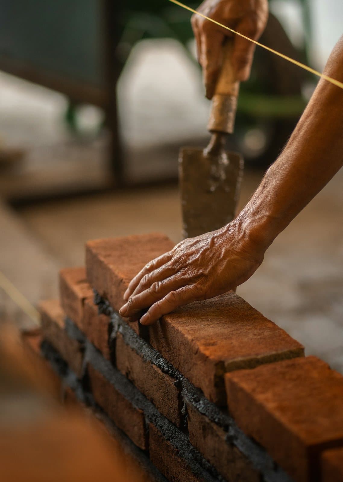 A bricklayer pressing a red brick into fresh mortar along a string line