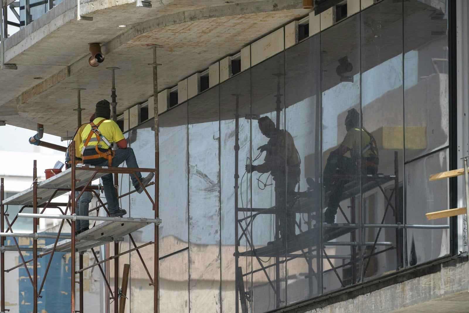 Glaziers on scaffolding fitting tall glass panels across the front of a building