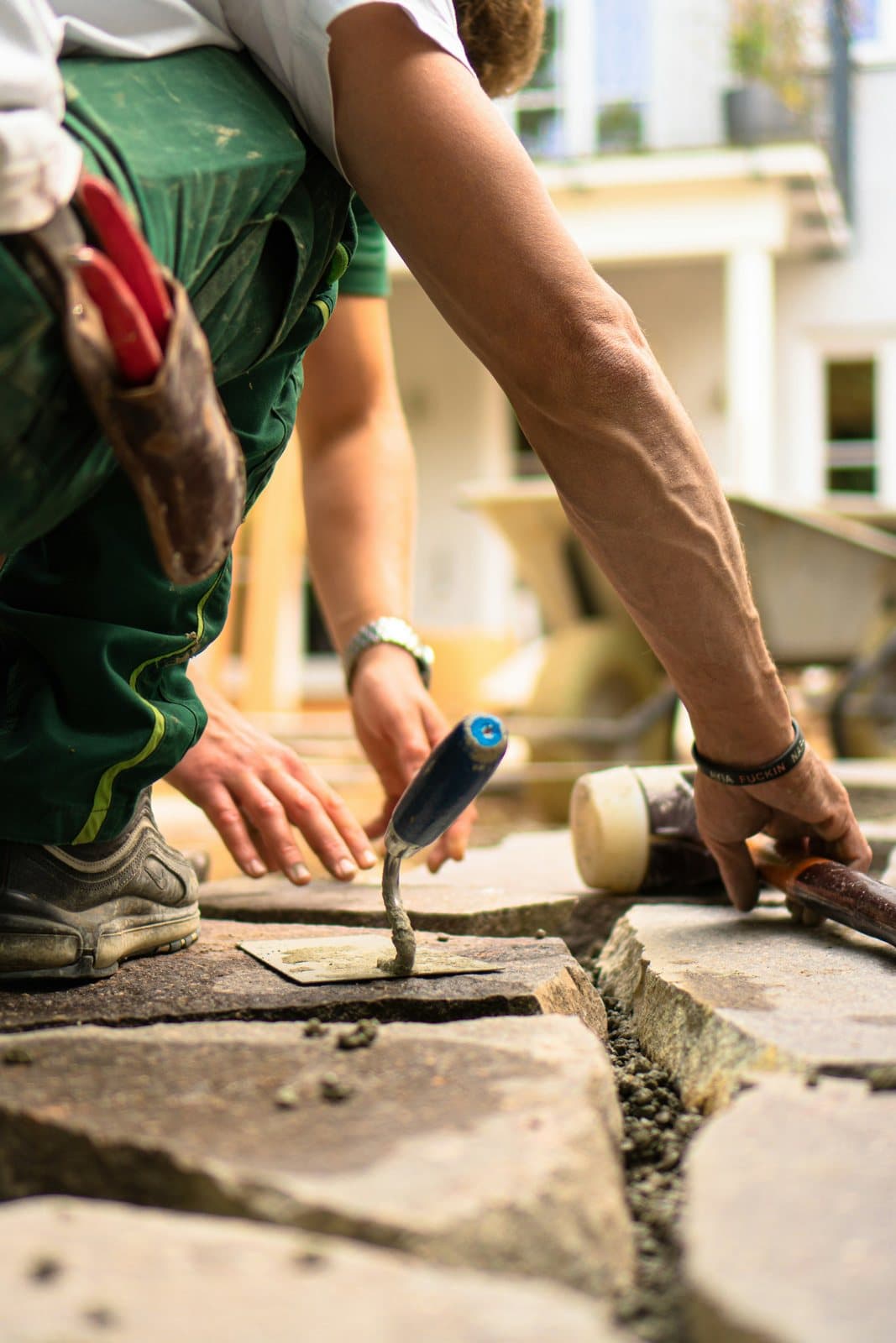 A landscaper setting sandstone paving with a trowel, a rubber mallet to hand