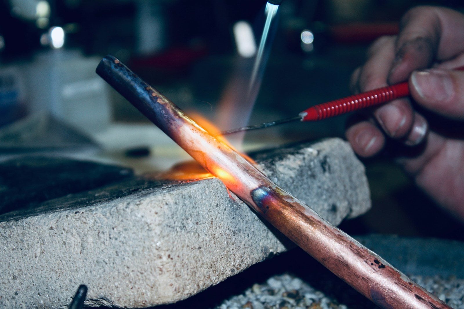A copper pipe glowing under a torch flame, with a thin rod held to the joint