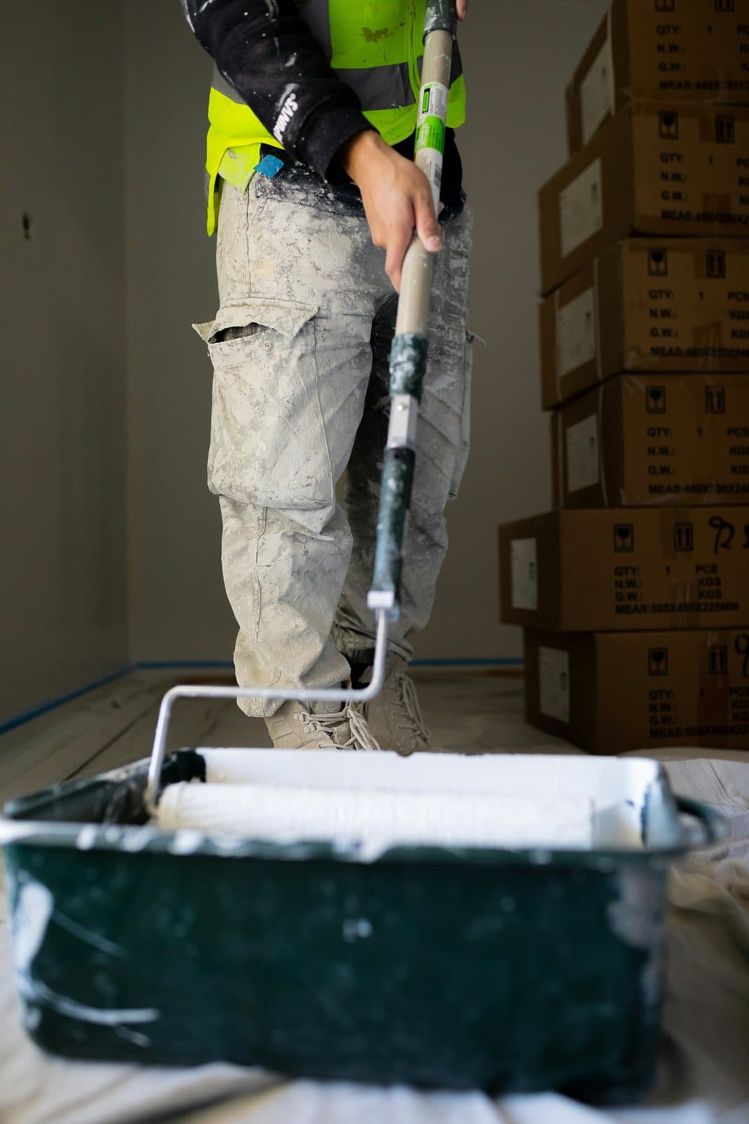 A worker in hi-vis loading a long-handled roller from a tray of coating